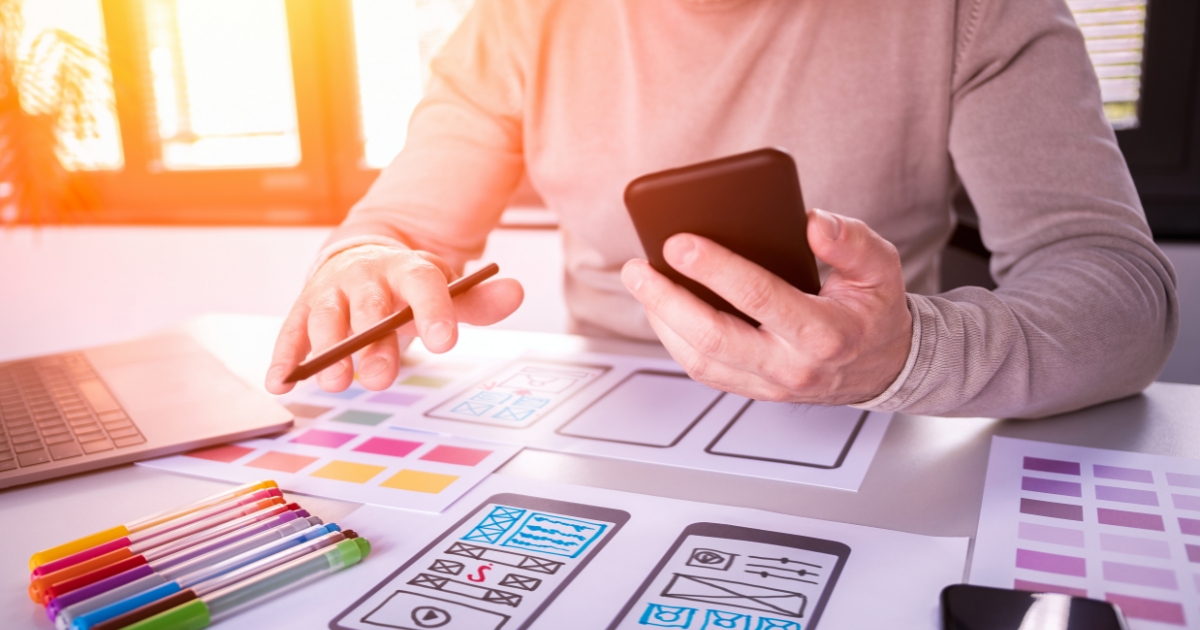 A person holding a smartphone showing a website wireframe.