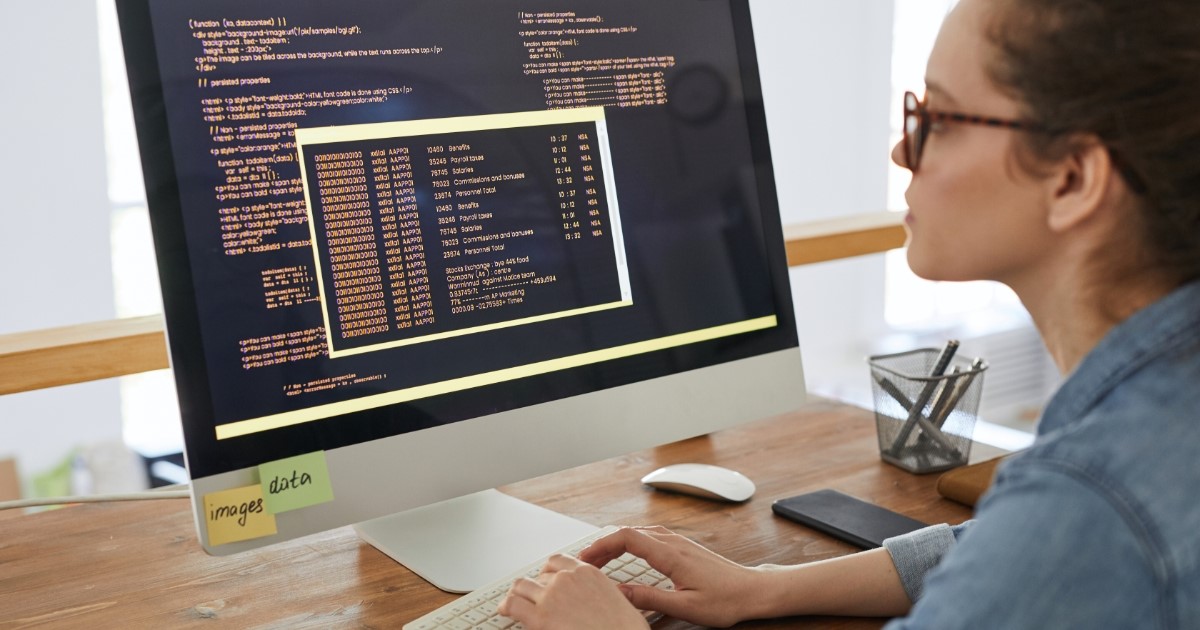 A woman standing in front of a computer screen with code, weighing the options between SaaS and custom software.